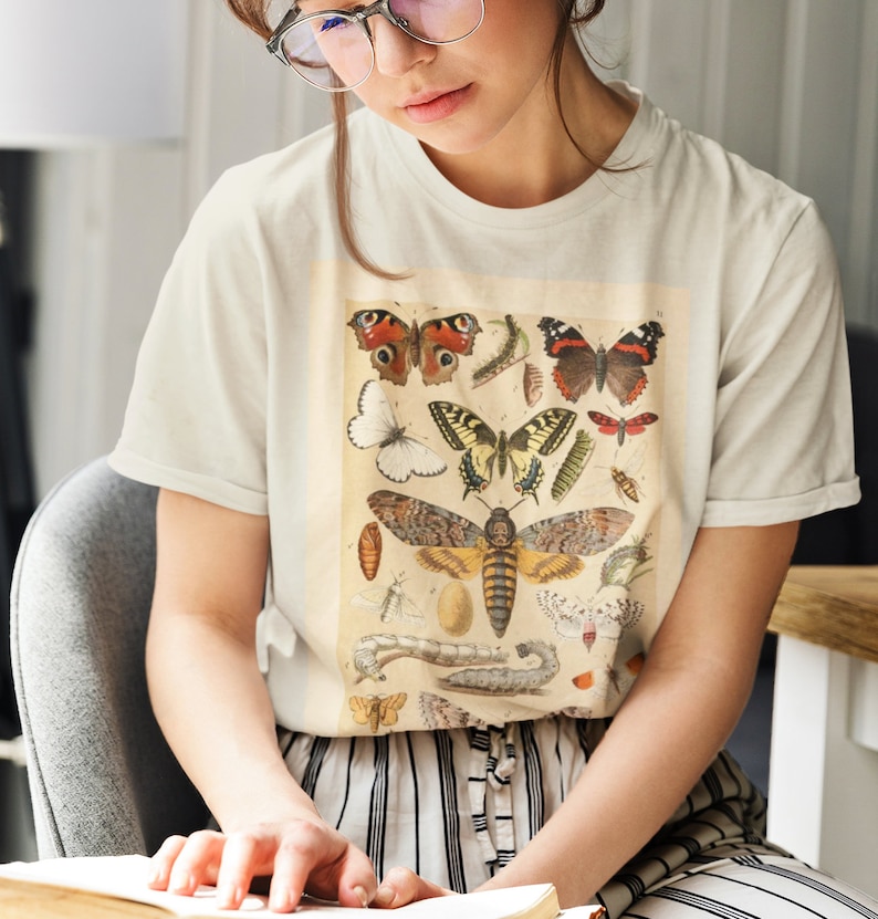 Op de afbeelding: Een wit T-shirt met een vintage illustratie van verschillende vlinders en motten. De illustratie is in tinten bruin, geel, oranje en zwart.
