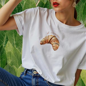 May include: White t-shirt with a brown croissant graphic and the text "il cornetto" in pink.