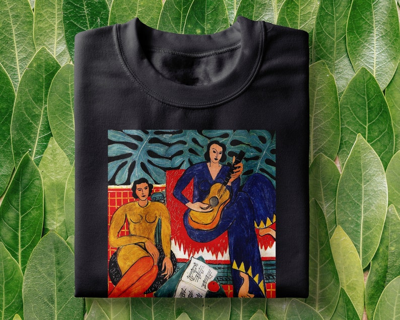Puede incluir: Camiseta negra con una pintura colorida de dos mujeres, una tocando la guitarra, en un entorno de jungla. La pintura incluye un esquema de color rojo, amarillo y azul.