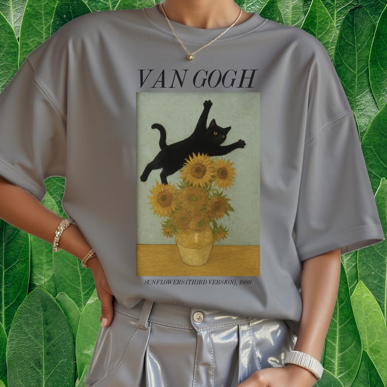 以下が含まれることがあります： 黒猫がひまわりの花瓶の上を跳ねている灰色のTシャツ。ゴッホの「ひまわり」のパロディ。画像の上には「VAN GOGH」、下には「SUNFLOWERS (THIRD VERSION), 1888」と書かれています。