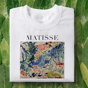 Pode incluir: Camiseta branca com uma pintura abstrata colorida de Henri Matisse e o texto "MATISSE" impresso na frente.