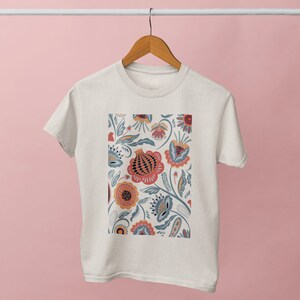 May include: A white t-shirt with a floral print featuring red, orange, yellow, blue, and green flowers. The flowers are stylized and have a folk art aesthetic.