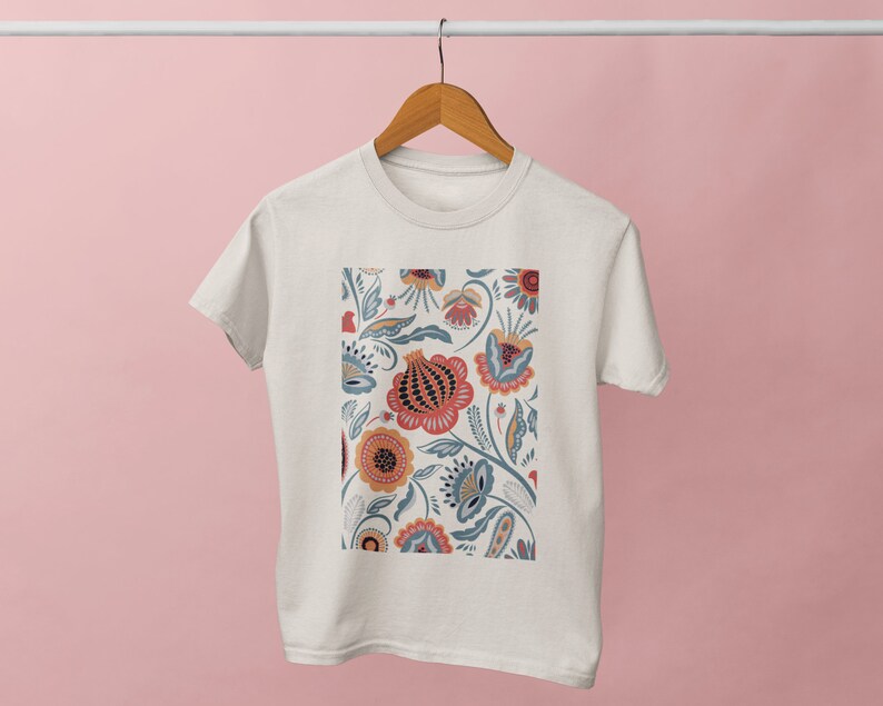 May include: A white t-shirt with a floral print featuring red, orange, yellow, blue, and green flowers. The flowers are stylized and have a folk art aesthetic.