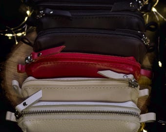 May include: Four leather zippered pouches in different colors: black, brown, red, and cream. The pouches are stacked on top of each other.