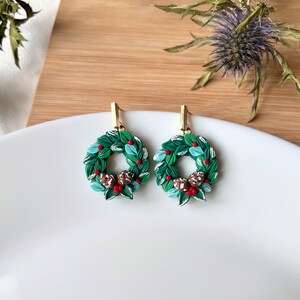 May include: A pair of green, red, and brown Christmas wreath earrings with gold hooks.