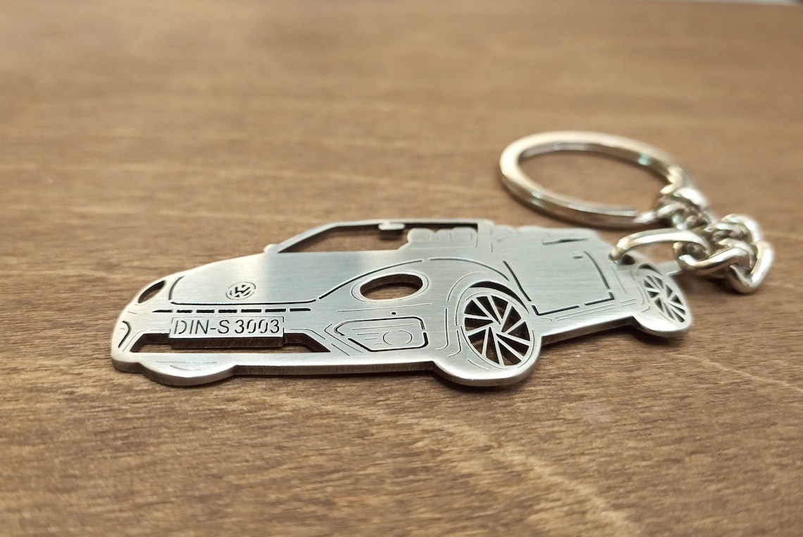  A silver metal keychain in the shape of a motorbike with the text "DIN-S 3003" on the license plate.