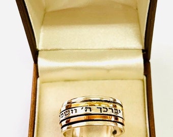 May include: A silver and gold spinning ring with Hebrew text inscribed on the band. The ring is in a brown box with a white interior.