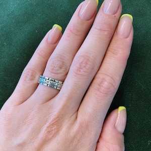 May include: A hand wearing a silver ring inscribed with Hebrew writing. The fingernails are painted with a light pink polish and have yellow tips.