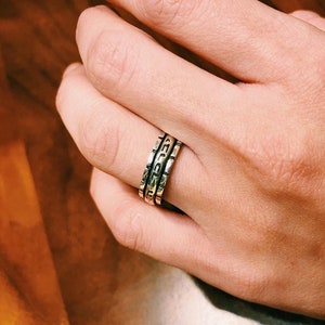 May include: A silver ring with three bands, each with a different inscription. The bands are stacked on top of each other.