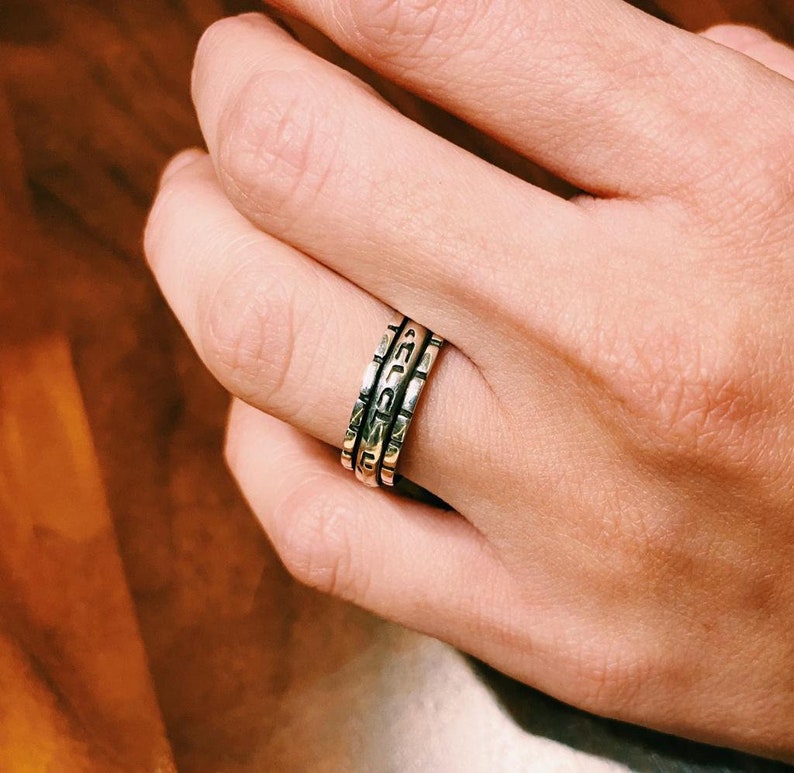 May include: A silver ring with three bands, each with a different inscription. The bands are stacked on top of each other.