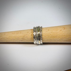 May include: A silver and gold spinning ring with a textured design. The ring is made of multiple bands that spin independently.
