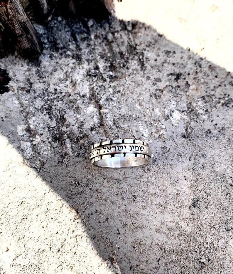 May include: A silver ring with Hebrew text engraved around the band. The text reads "Shema Yisrael Adonai Eloheinu Adonai Echad" which translates to "Hear O Israel, the Lord our God, the Lord is One."