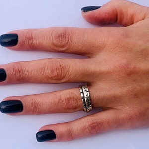 May include: A hand with black nail polish is wearing a silver ring with a textured design. The ring is made of three bands stacked together.
