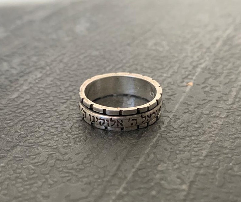 May include: A silver ring with Hebrew text inscribed around the band.