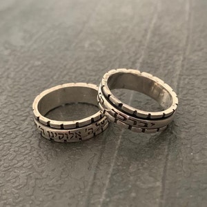 May include: Two silver rings with Hebrew text engraved on the bands. The rings are stacked on top of each other.
