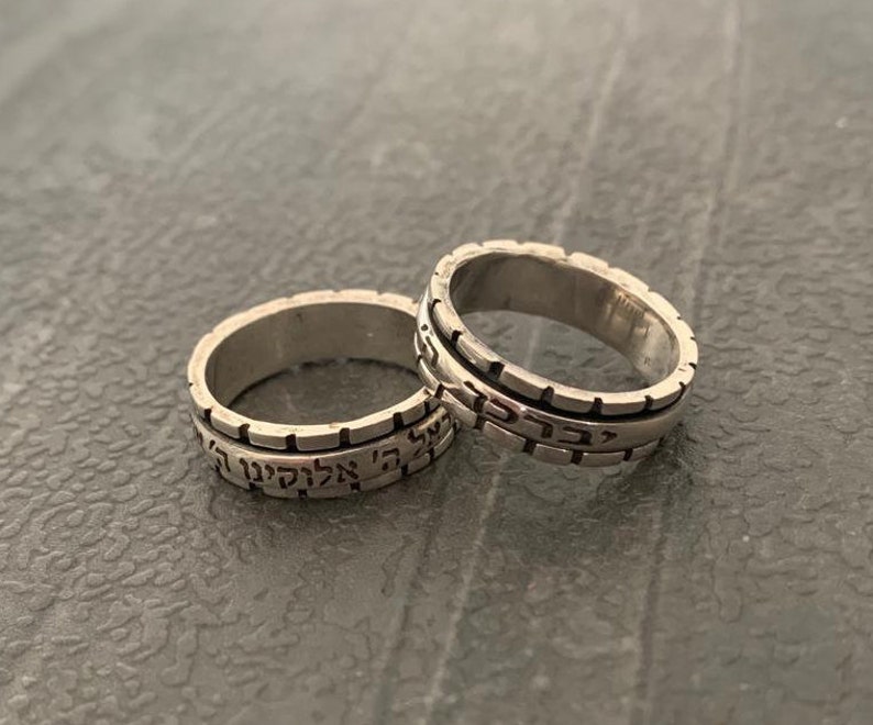 May include: Two silver rings with Hebrew text engraved on the bands. The rings are stacked on top of each other.