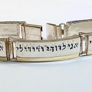 May include: A silver bracelet with a gold band and Hebrew writing. The bracelet is made of multiple links, each with a different inscription.