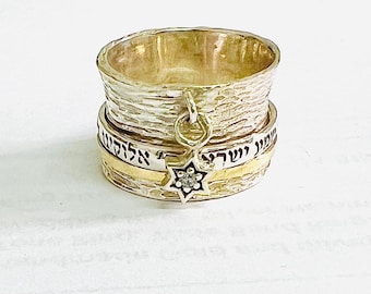 May include: A silver spinning ring with a gold band and a charm with a star of David and a small diamond. The ring is inscribed with Hebrew text.