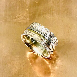May include: A silver ring with a textured design, featuring multiple bands that appear to be stacked on top of each other.