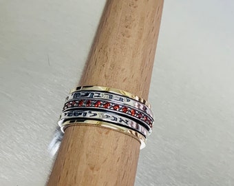 May include: A silver and gold spinning ring with a band of red gemstones. The ring has Hebrew writing on it.