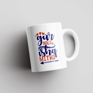 May include: White ceramic mug with a blue and orange design. The text on the mug reads "gur nalo" and "ishq mitha" with a small arrow.