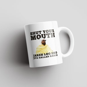 Pode incluir: Caneca de cerâmica branca com uma ilustração em preto e branco de um homem usando óculos de sol e uma túnica amarela. O texto "SHUT YOUR MOUTH JAREH LOG EHO JIYA GALLAN KARDE" está impresso na caneca.