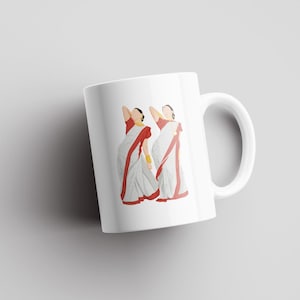 May include: White ceramic mug featuring a minimalist illustration of two figures in traditional Indian attire. The figures are depicted in white sarees with red borders, gold jewelry, and their arms raised. The mug has a curved handle.