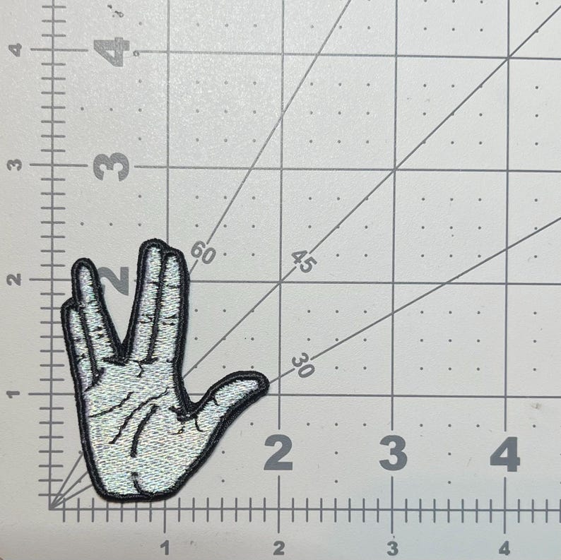 May include: A white and silver embroidered patch of a hand making the Vulcan salute, a popular gesture from the Star Trek franchise.