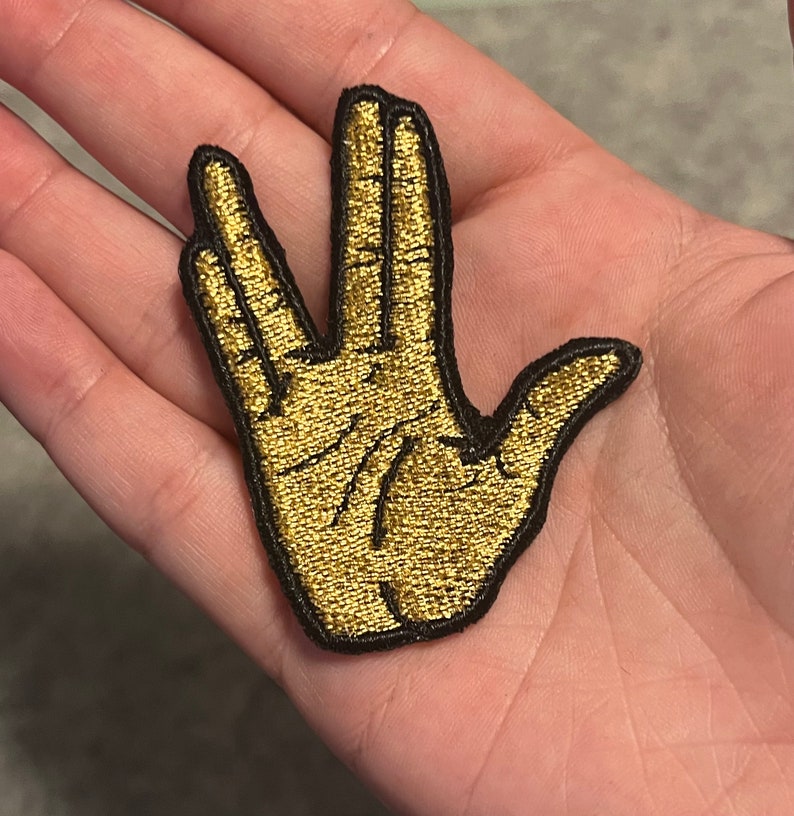 May include: Gold embroidered patch of the Vulcan salute hand gesture.