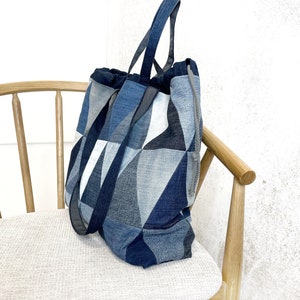Könnte beinhalten: Eine große blaue Jeans-Tragetasche mit Kordelzug und Patchwork-Design. Die Tasche ist aus verschiedenen Blautönen von Jeans gefertigt und hat ein geometrisches Muster.