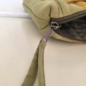 Green–mustard denim cosmetic bag displayed outdoors with natural light. Summer-inspired look for nature lovers, combining slow-crafted design and practical function.