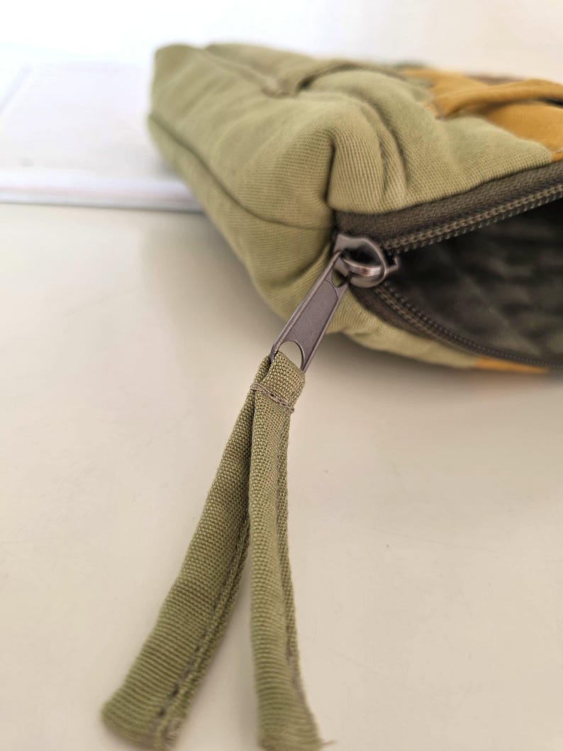 Green–mustard denim cosmetic bag displayed outdoors with natural light. Summer-inspired look for nature lovers, combining slow-crafted design and practical function.