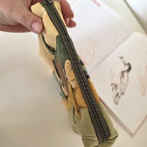 Top view of green–mustard denim makeup bag with smooth zipper and floral centre panel. One-of-a-kind padded accessory pouch for travel minis, small tech items or everyday organisation.