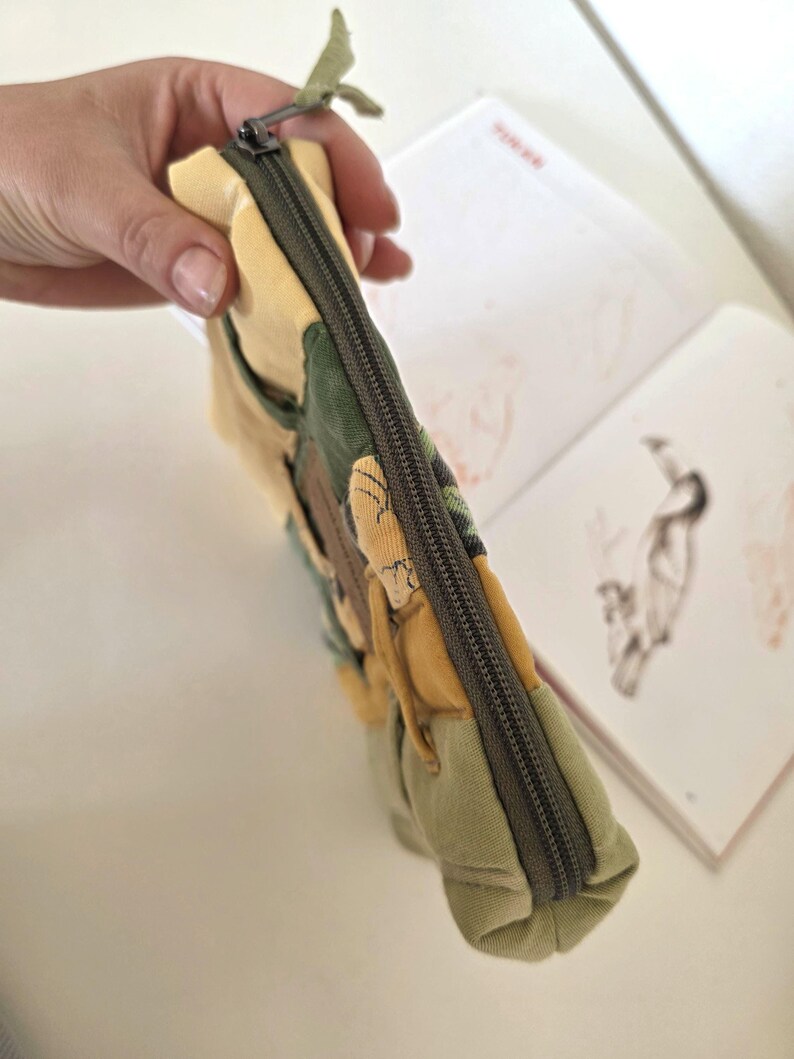 Top view of green–mustard denim makeup bag with smooth zipper and floral centre panel. One-of-a-kind padded accessory pouch for travel minis, small tech items or everyday organisation.