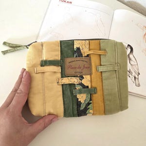 Upcycled denim cosmetic pouch in green and mustard tones with one floral accent strip, photographed close-up. Softly padded, neatly stitched zipper bag designed for makeup, stationery or daily essentials.