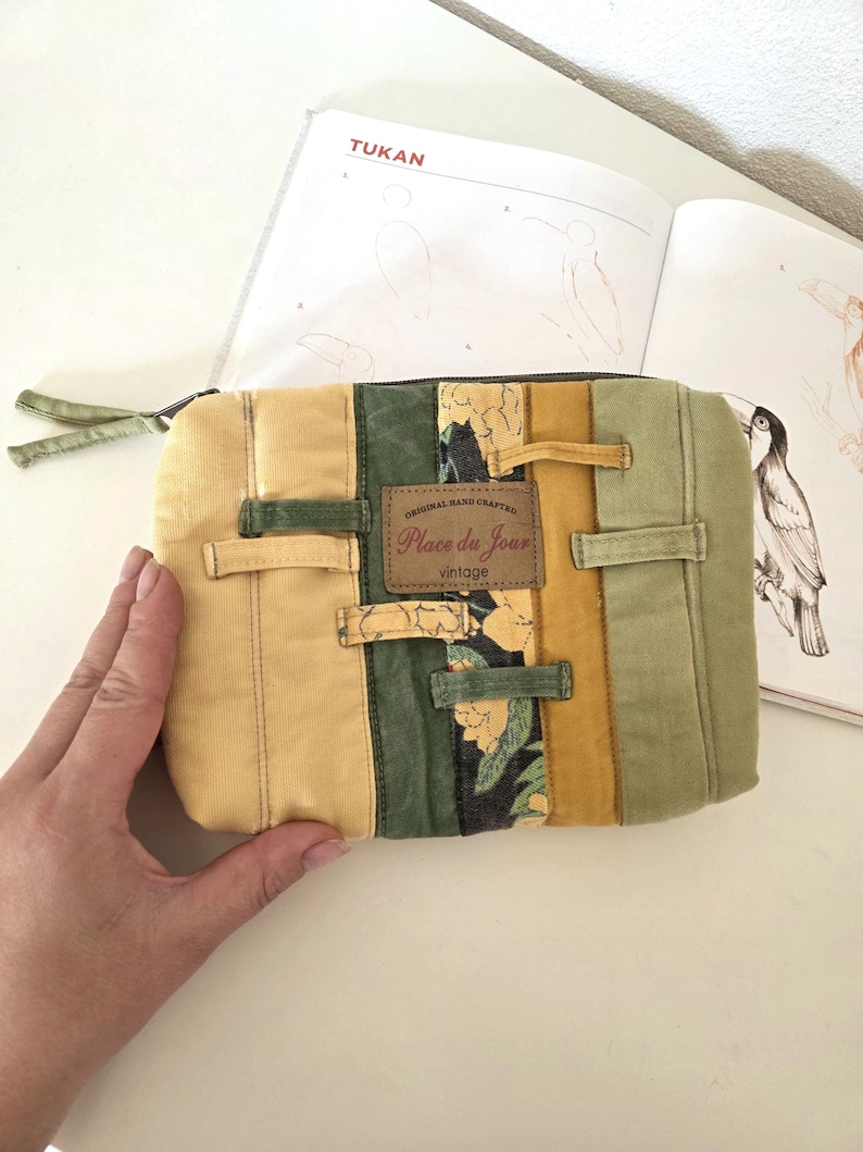 Upcycled denim cosmetic pouch in green and mustard tones with one floral accent strip, photographed close-up. Softly padded, neatly stitched zipper bag designed for makeup, stationery or daily essentials.