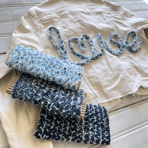 Può includere: Una giacca di jeans beige chiaro con la parola "love" cucita sul retro in denim blu. Tre rotoli di nastro di jeans blu sono in primo piano, ognuno con una diversa tonalità di blu.