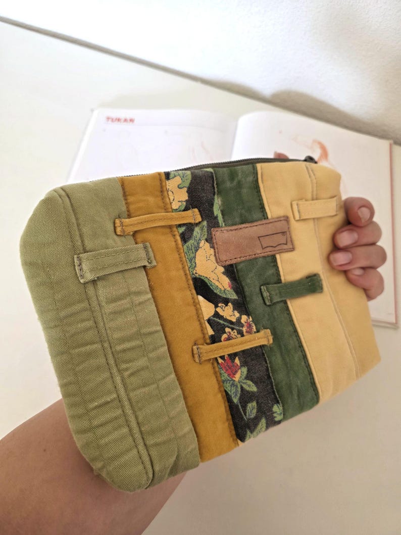 Repurposed denim zipper pouch made from waistbands and belt loops, featuring water-repellent lining. Unique floral detail adds a soft summer mood, ideal for slow living and eco-minded users.