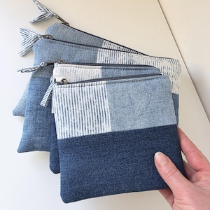 Könnte beinhalten: Vier Jeans-Reißverschlusstaschen in verschiedenen Blautönen. Jede Tasche kombiniert einfarbigen und gestreiften Denim. Die Taschen haben silberne Reißverschlüsse und gestreifte Stoff-Reißverschlussanhänger.