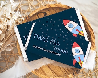 May include: Two chocolate bar wrappers with a blue background and white stars. The wrappers feature a rocket ship and the text "Two the moon Austin's 2nd Birthday".