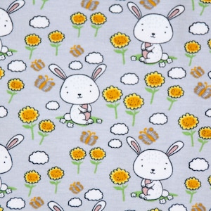 Könnte beinhalten: Ein grauer Stoff mit einem sich wiederholenden Muster aus weißen Kaninchen, die gelbe Blumen, gelbe Sonnenblumen und Schmetterlinge halten.