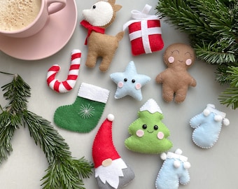 May include: A set of felt Christmas ornaments, including a reindeer, a candy cane, a stocking, a gingerbread person, a star, a Christmas tree, a gnome, and two mittens. The ornaments are all in various colors, including red, green, blue, brown, and white. The text "Pdf pattern" is written in pink letters on a white background.