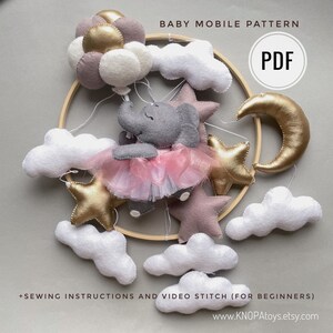 May include: A handmade baby mobile pattern featuring a gray elephant wearing a pink tutu, surrounded by felt stars, clouds, and a gold crescent moon. The mobile includes the text "BABY MOBILE PATTERN" and "PDF".