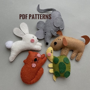 Peut inclure: Cinq jouets en feutre en forme d'animaux : une souris grise, un lapin blanc, un chien brun, un chat orange et une tortue verte. Les jouets sont disposés en cercle sur un fond gris. Le texte « PDF PATTERNS » est écrit en lettres brunes en haut de l'image.