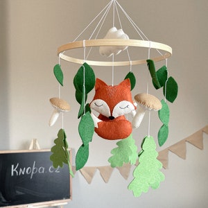 Peut inclure: Un mobile bébé en bois avec un renard, des feuilles, des champignons et des nuages. Le mobile est fait de feutre et est suspendu à un anneau en bois.
