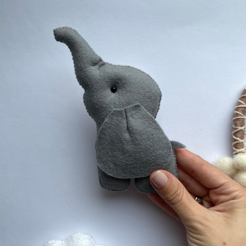 K&ouml;nnte beinhalten: Ein graues Filz-Elefantenspielzeug mit einem schwarzen Knopfauge. Der Elefant steht auf seinen vier Beinen und hat einen langen R&uuml;ssel.