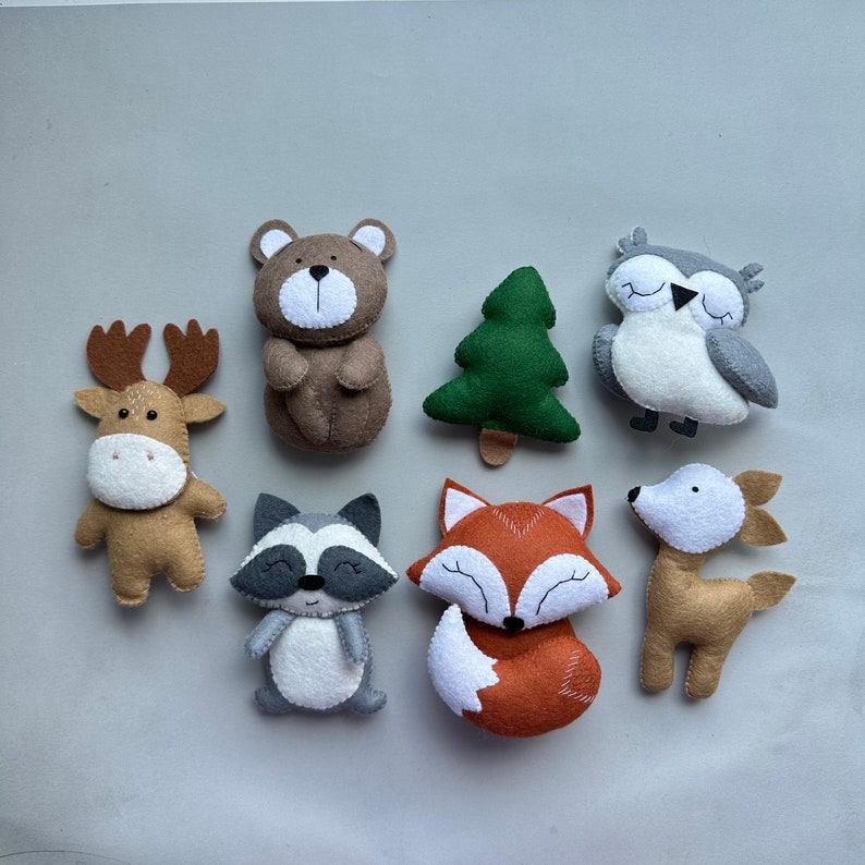 May include: A set of felt woodland animal toys, including a brown bear, a deer, a raccoon, a fox, an owl, and a green tree. The toys are all handmade and have embroidered details.