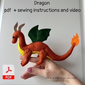 May include: A handmade felt dragon toy in shades of orange, yellow, and green. The dragon has a long tail with an orange flame, green wings, and brown horns. The text "Dragon pdf + sewing instructions and video" is at the top.