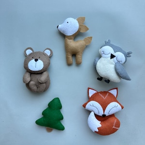 May include: Five felt animal toys, including a brown bear, a brown deer, a gray owl, an orange fox, and a green Christmas tree. The toys are all handmade and have a simple, whimsical design.