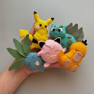 May include: A set of felt plush toys featuring popular Pokemon characters, including Pikachu, Bulbasaur, Squirtle, Charmander, and Jigglypuff. The toys are brightly colored and have embroidered details.